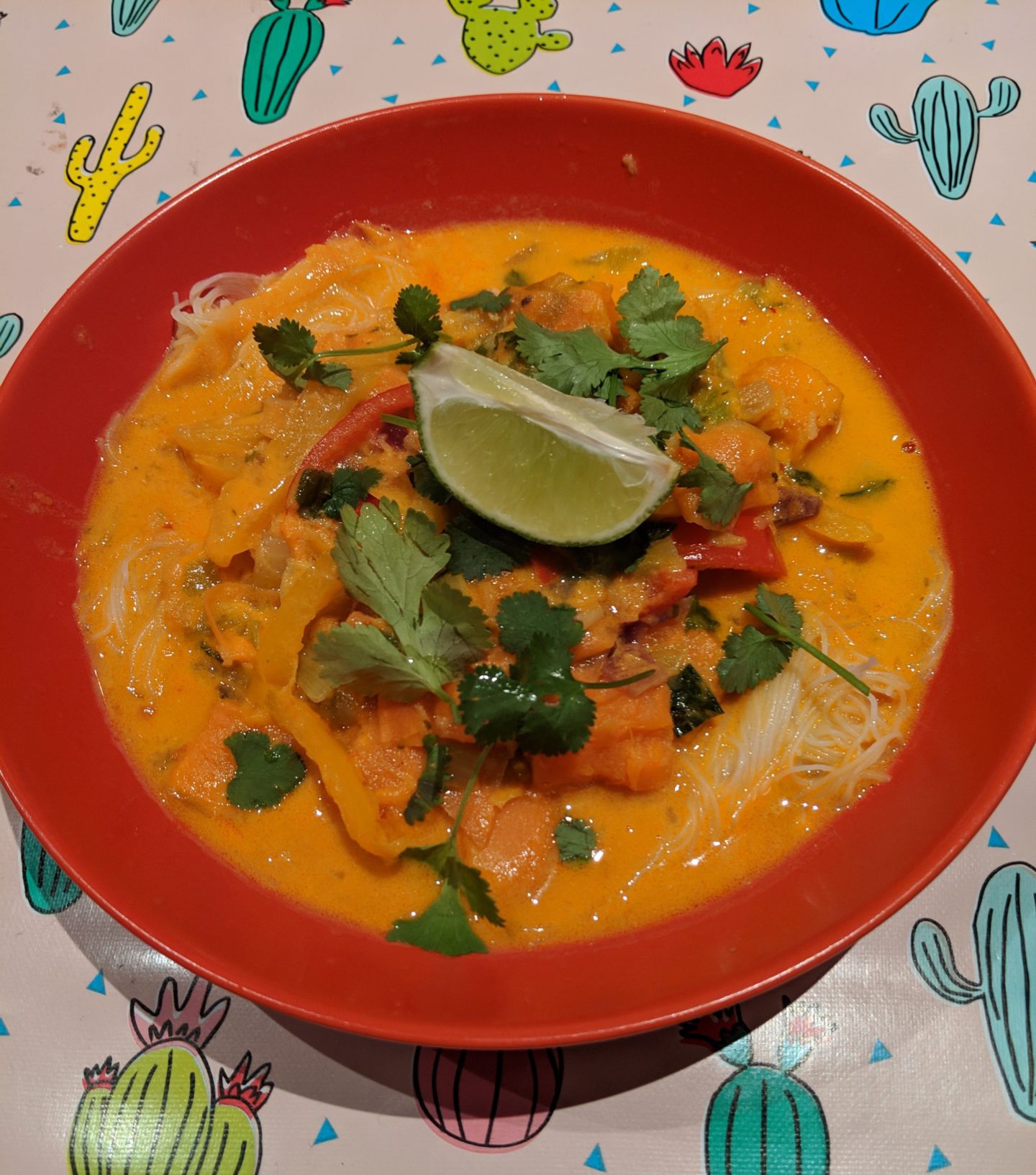 close up red bowl containing thai noodle soup with vegetables and lime