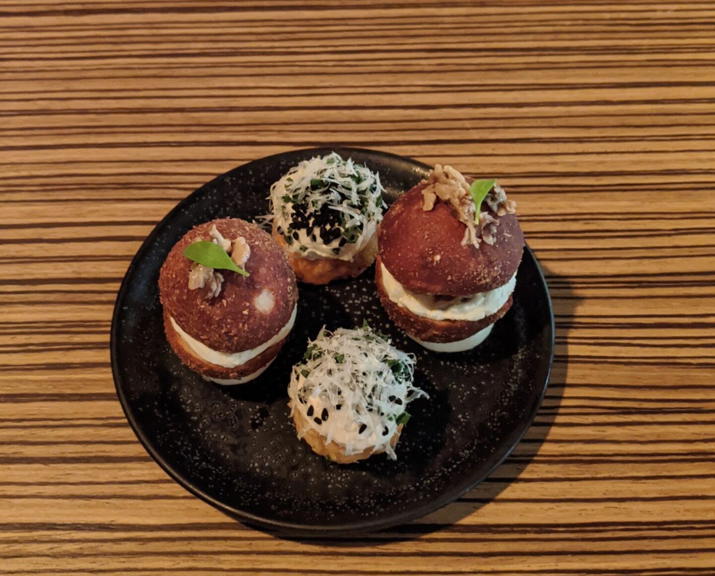 Black plate on wooden table showing 4 starters of food from Etch